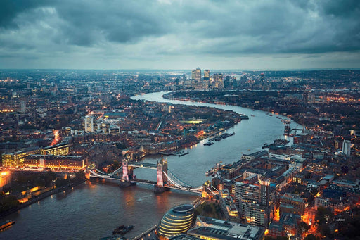 Aerial view of a cityscape with a river and bridge under a cloudy sky.